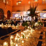 Corporate event theme "Catching Fire" features gold dazzle table linen, black chair covers and napkins, grass and feather-based centerpieces, and candlelight.